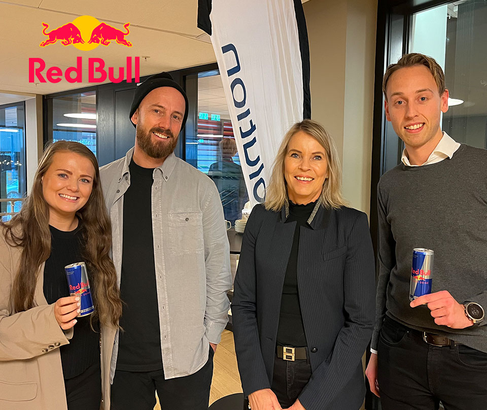 Fire blide mennesker, 2 kvinner og 2 menn står ved siden av hverandre og ser inn i kamera. Bak vimpel med Tradesolution logo og Red Bull logo. Foto